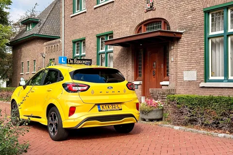 De gele Ford Puma van De Rijkoning met dakbord bij een bakstenen huis