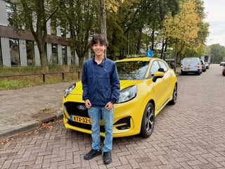 Geslaagde jongen naast de nieuwe gele Ford Puma met dakbord