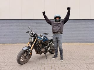 Geslaagde motorrijder met de armen omhoog naast de Honda