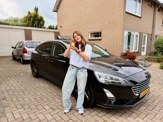 Geslaagde jonge vrouw bij de zwarte lesauto