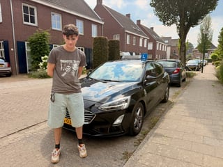 Geslaagde jongen bij de zwarte lesauto