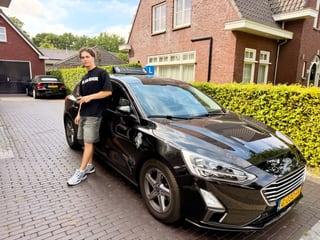 Geslaagde jongen voor de lesauto in een woonstraat