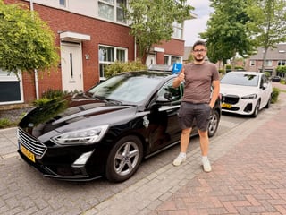 Geslaagde jongen naast de zwarte lesauto