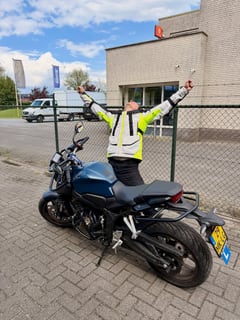 Geslaagde motorleerling in geel hesje met de armen omhoog