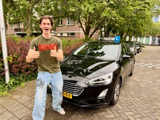 Geslaagde jongen met duimen omhoog bij de lesauto