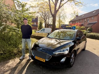 Geslaagde jongen voor de lesauto met dakbord