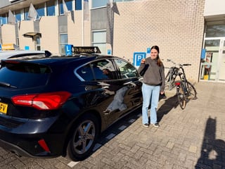 Geslaagde jonge vrouw naast de lesauto en haar fiets
