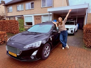 Geslaagde jonge vrouw met de arm omhoog naast de lesauto