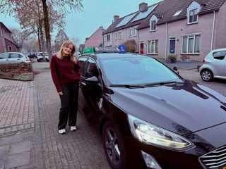 Geslaagde jonge vrouw tegen de lesauto