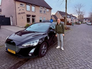 Geslaagde jongen naast de lesauto in een straat met oude huizen