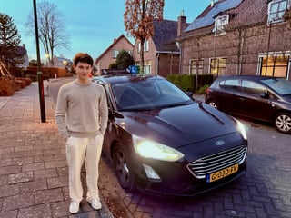 Geslaagde jongen bij de lesauto met de koplampen aan