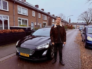 Geslaagde jongen in een bruine jas bij de lesauto