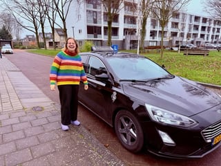 Geslaagde jonge vrouw in een gestreepte trui bij de lesauto