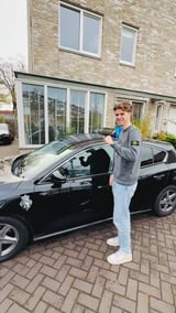Geslaagde jongen bij het geopende portier van de lesauto