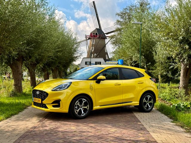 De gele Ford Puma van De Rijkoning met dakbord voor een molen