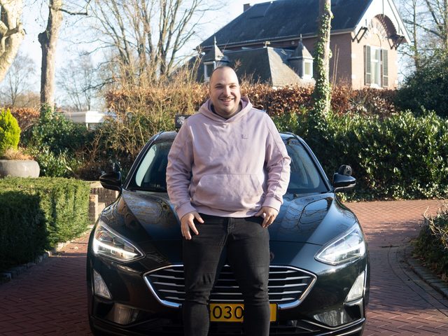 Bjorn van Lierop in een roze hoodie voor de zwarte lesauto