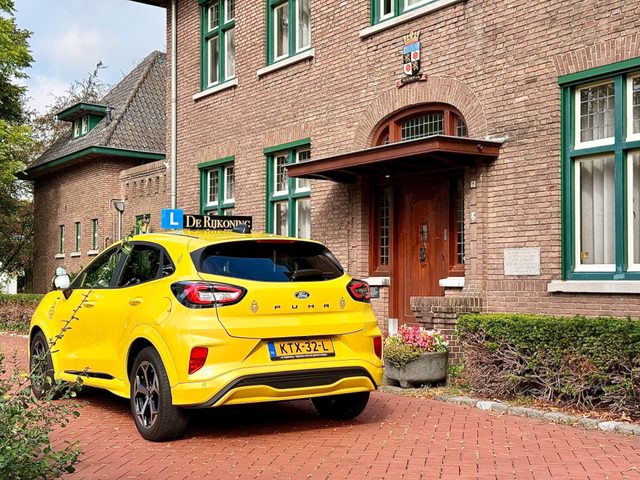 De gele Ford Puma van De Rijkoning met dakbord bij een bakstenen huis